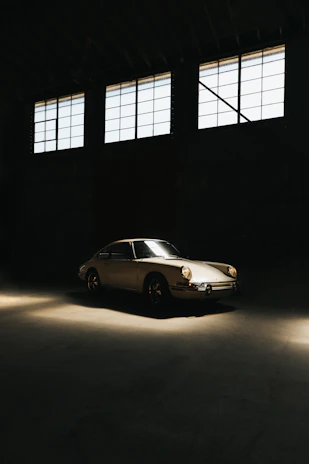 A gleaming restored 1960s Jaguar E-Type parked under soft golden lighting in the classic garage.