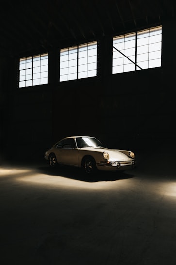 A vintage car parked in a sunlit garage with paperwork and a title document on a wooden table nearby.