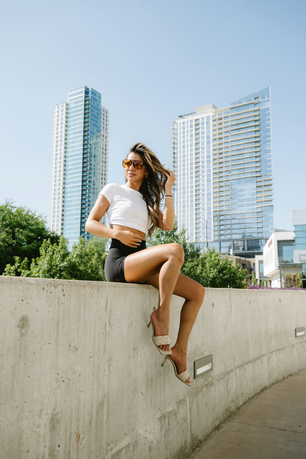 a woman sitting on a wall in a white shirt and black shorts