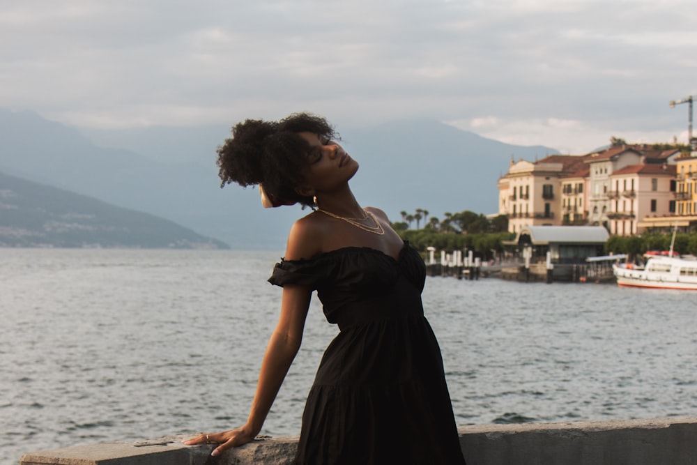 a woman in a black dress leaning on a wall