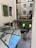 An interior courtyard featuring vertical gardens growing on the walls, large glass windows showcasing reflections, and a seating area with tables and chairs. Two tall, sculptural floor lamps enhance the modern design. The floor is tiled, adding a geometric pattern to the overall clean aesthetics.