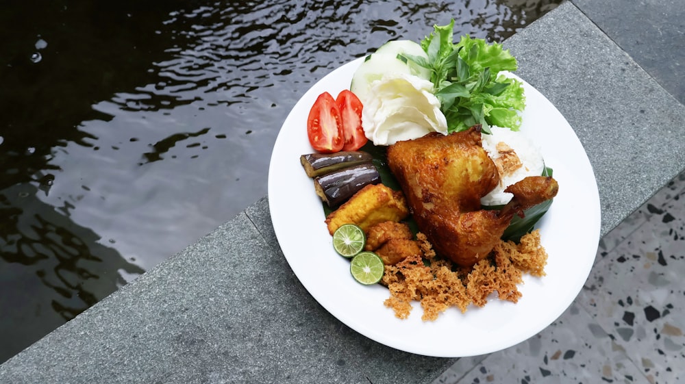 un plato blanco cubierto con carne y verduras junto a un cuerpo de agua