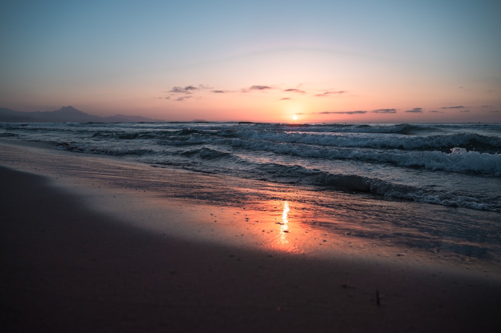 the sun is setting over the ocean on the beach