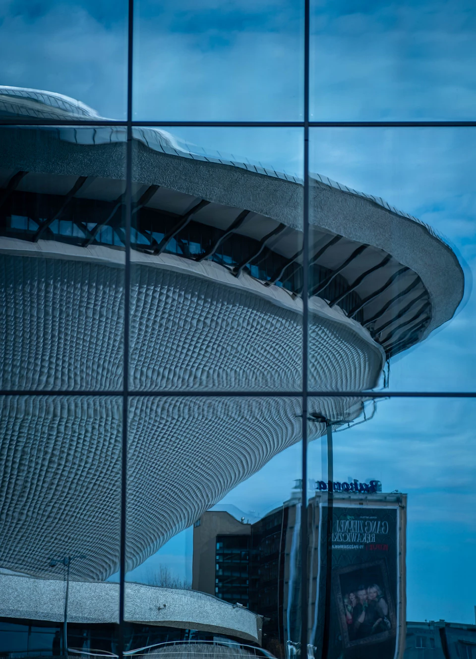 Large modern building with curved roof and glass facade dominates urban landscape from below