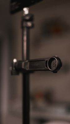 A close-up image of a metal stand with a clamp labeled 'GUARD LOCK.' The background is blurred, giving a shallow depth of field effect.