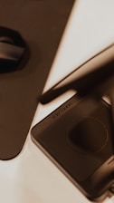 A close-up view of a digital drawing tablet with a stylus resting on it. The design appears sleek and modern with a predominantly black surface, highlighted by the presence of a circular touchpad. The lighting gives it a warm and focused look, with shadows creating a subtle dramatic effect.