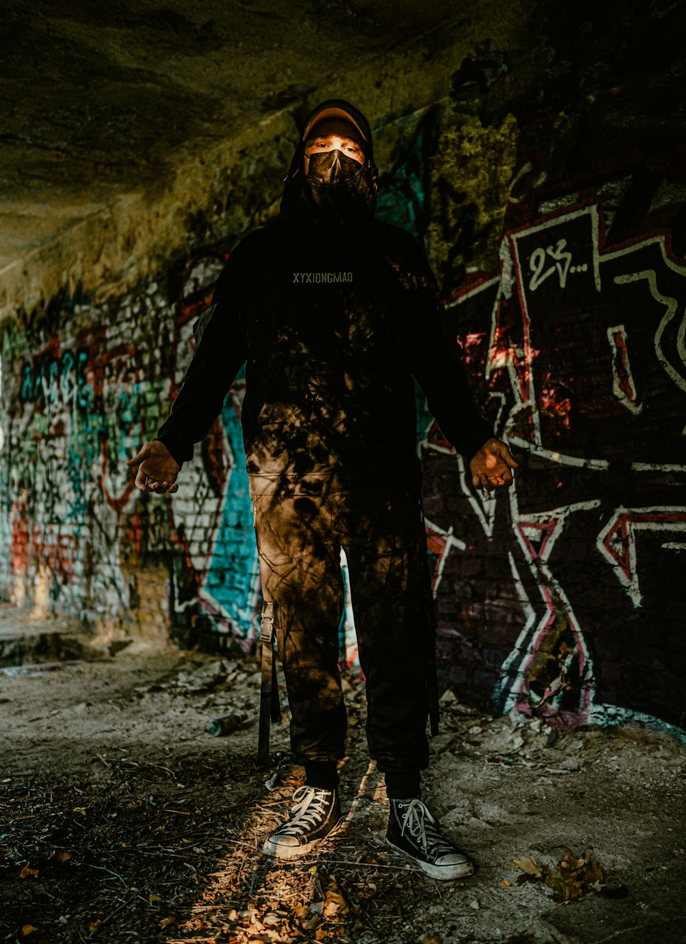 a man with a beard standing in front of a graffiti covered wall