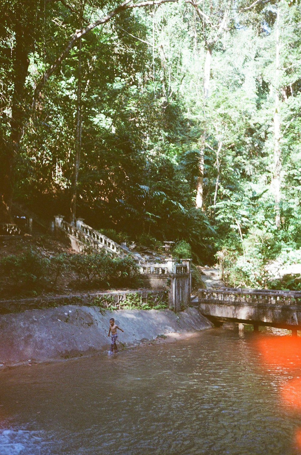 a person wading in a river near a bridge