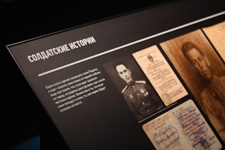 A display board features black-and-white photographs and documents. The documents include official papers and a portrait of a soldier. The text is in Cyrillic script and appears to relate stories about soldiers.