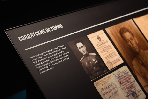 A display board features black-and-white photographs and documents. The documents include official papers and a portrait of a soldier. The text is in Cyrillic script and appears to relate stories about soldiers.