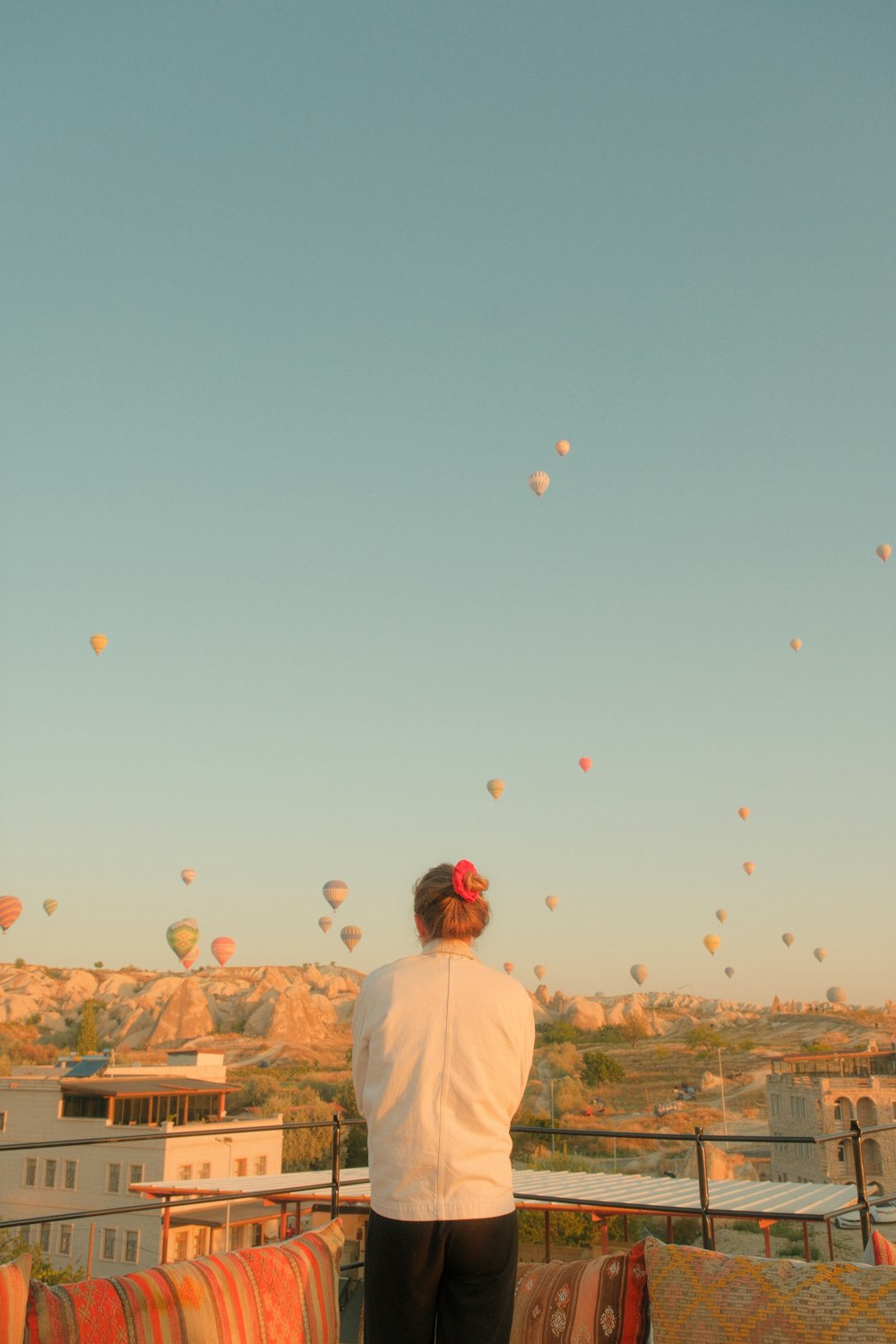 a woman standing on top of a roof watching hot air balloons