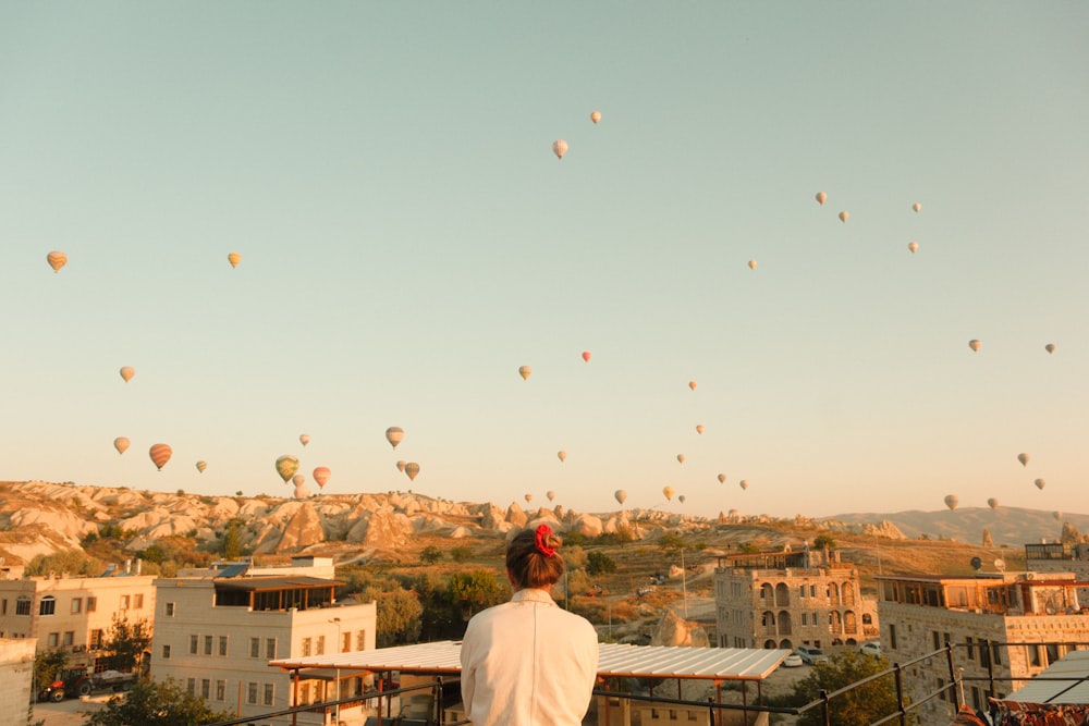 uma pessoa em pé em uma varanda olhando para balões de ar quente no céu