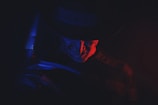 A sinister figure is partially illuminated by a dramatic play of red and blue lighting. The figure wears a dark hat and has a menacing expression, evoking a sense of fear and mystery.