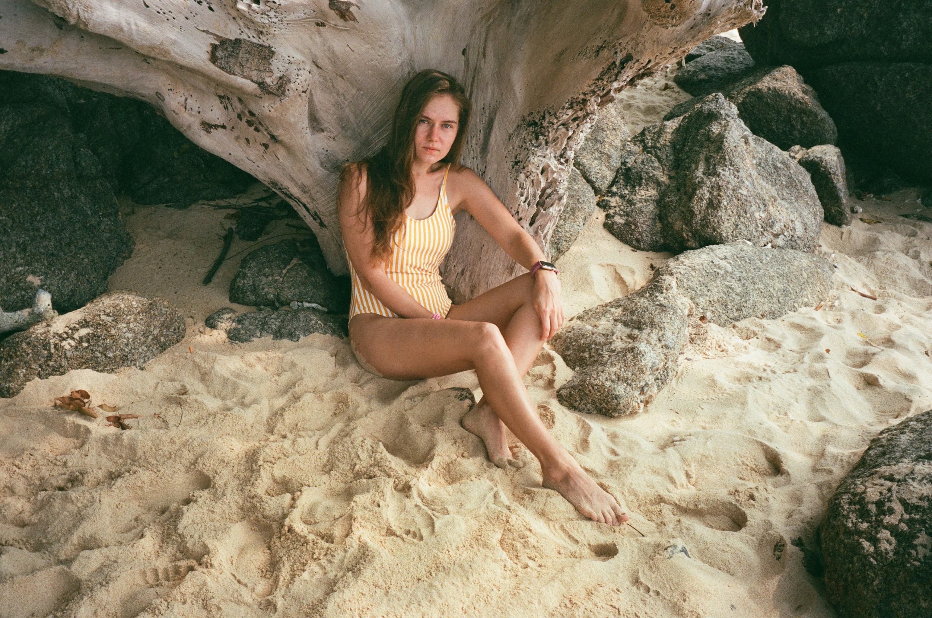 a woman sitting in the sand near a tree