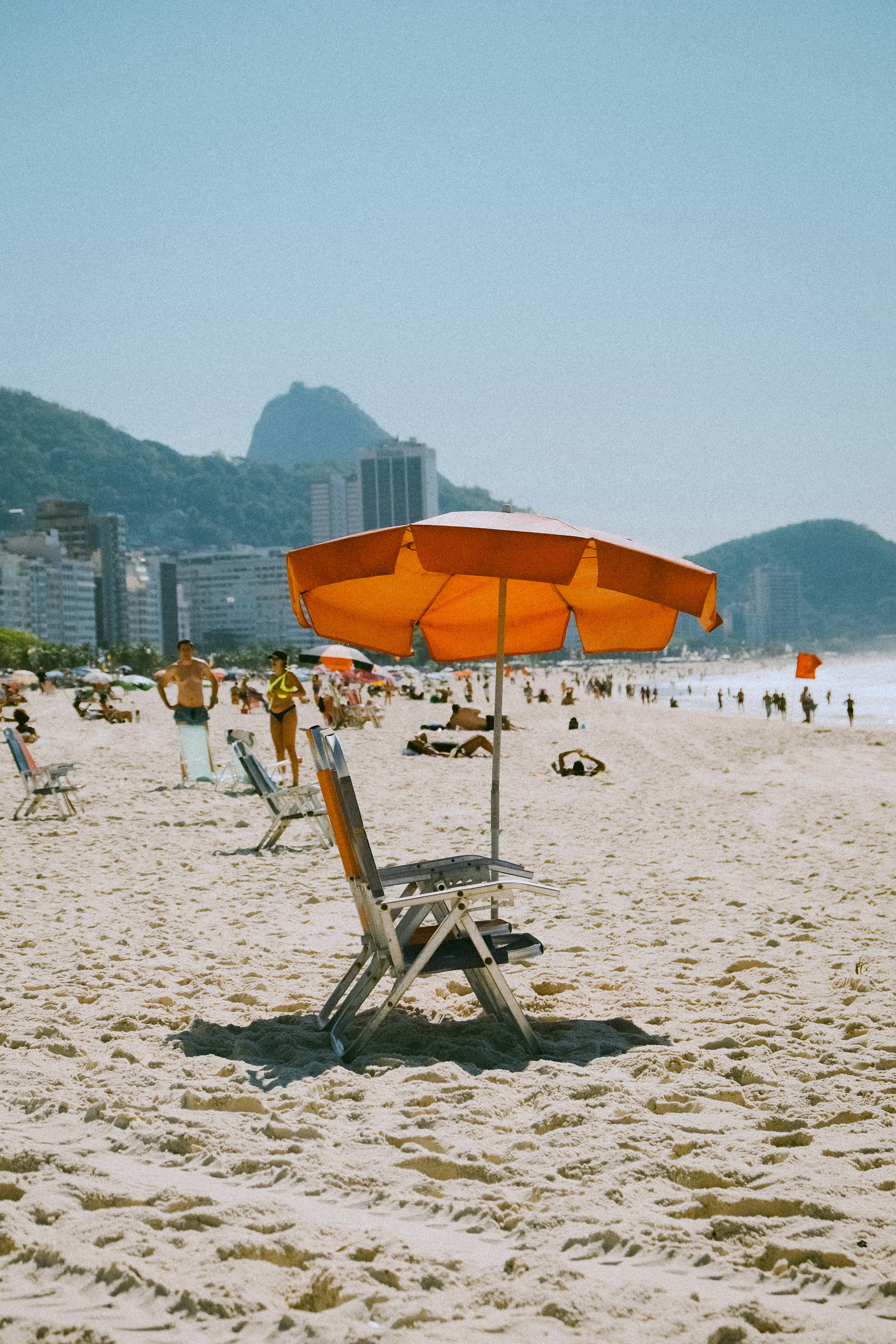 a chair and umbrella on a beach with people in the background
