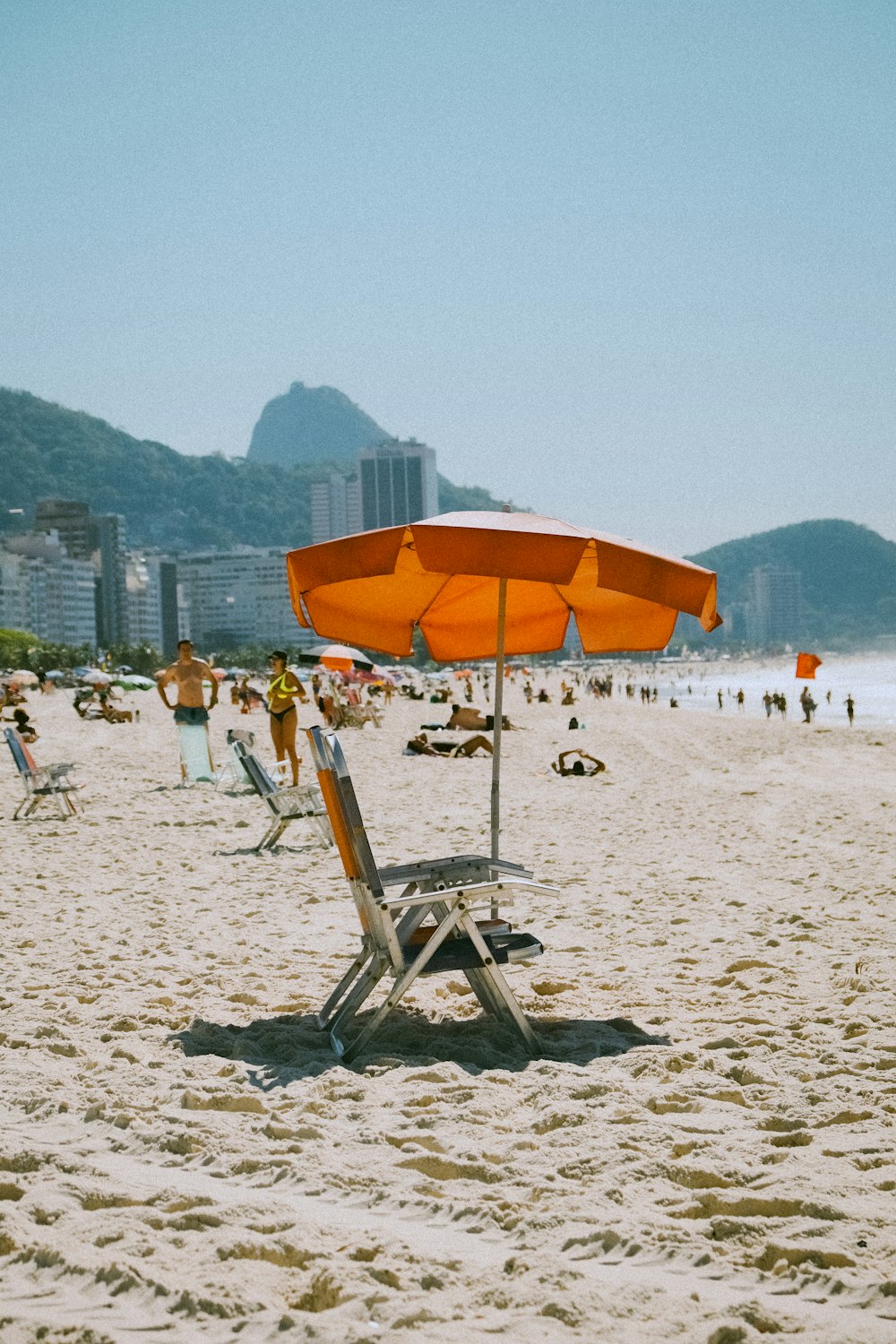 a chair and umbrella on a beach with people in the background