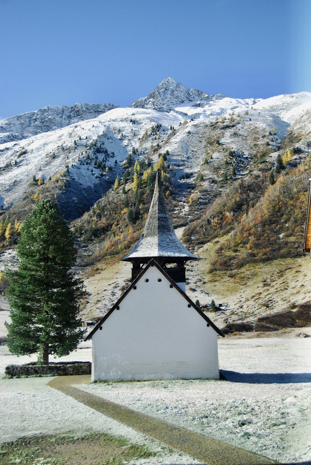 a small white building with a steeple in front of a snowy mountain