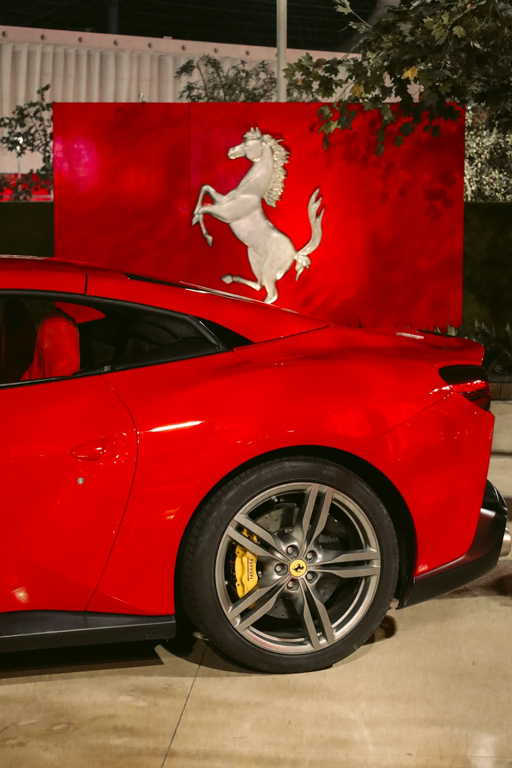 Um carro esportivo vermelho estacionado em frente a um logotipo da Ferrari