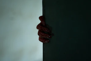 Close-up of a bloodied hand gripping a cleaver, the dark background adding to the suspense.