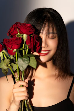 A warm portrait of Sophia Maria holding a bouquet of red roses and white flowers, smiling gently.