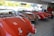 A showroom displays a collection of classic convertible cars with shiny exteriors. The bright lighting highlights the sleek, vintage design. The cars are parked closely together on a tiled floor, with large windows allowing natural light to filter in, revealing greenery outside.
