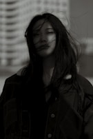 Profile shot of a woman with wind-blown hair, set against an urban backdrop.