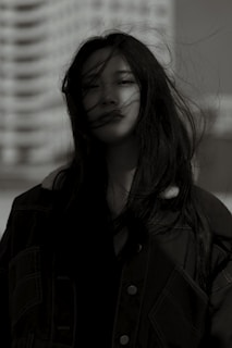Profile shot of a woman with wind-blown hair, set against an urban backdrop.