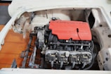 A partially disassembled car with a visible engine compartment. The centerpiece is a red engine cover with the word 'Corvette' and '5.7L' prominently displayed, indicating a V8 engine. The engine is installed within a chassis with a bare metal and unfinished body frame surrounding it.