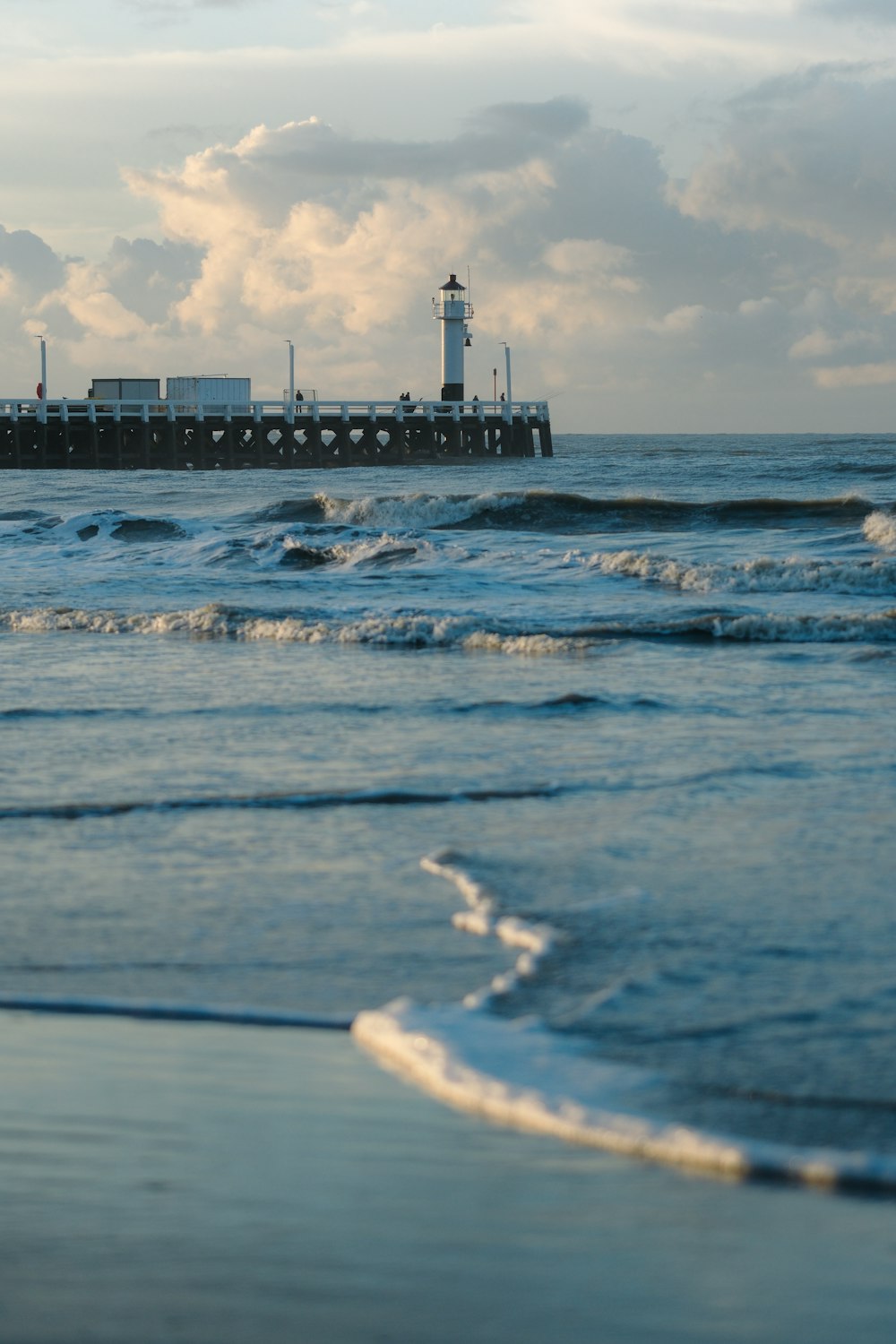 a beach with waves and a pier in the background