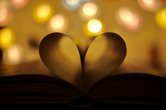 An open book with a heart-shaped bookmark resting on a cozy table.