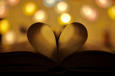 An open book with a heart-shaped bookmark resting on a cozy table.