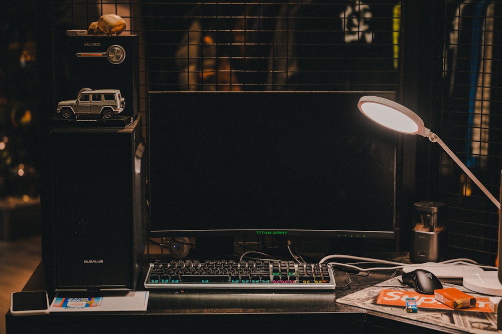 a desk with a keyboard, monitor, mouse and a lamp
