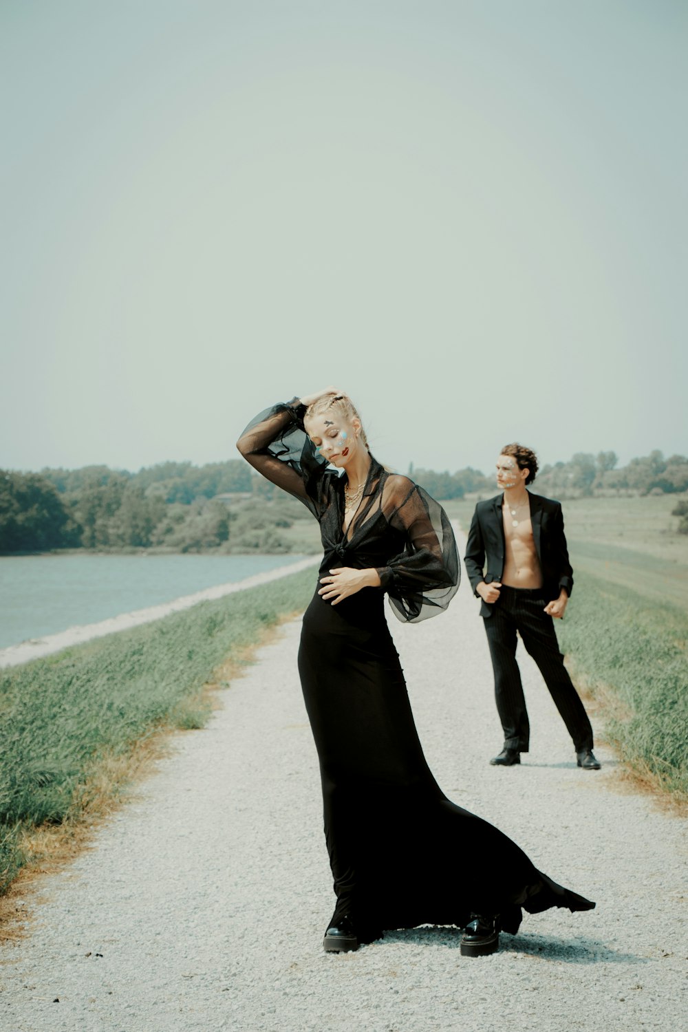 a woman in a long black dress standing on a dirt road