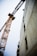 A towering construction crane next to a partially built concrete structure. The crane is orange with an intricate lattice framework. The building appears to be in the initial stages of development with visible scaffolding and open window spaces.