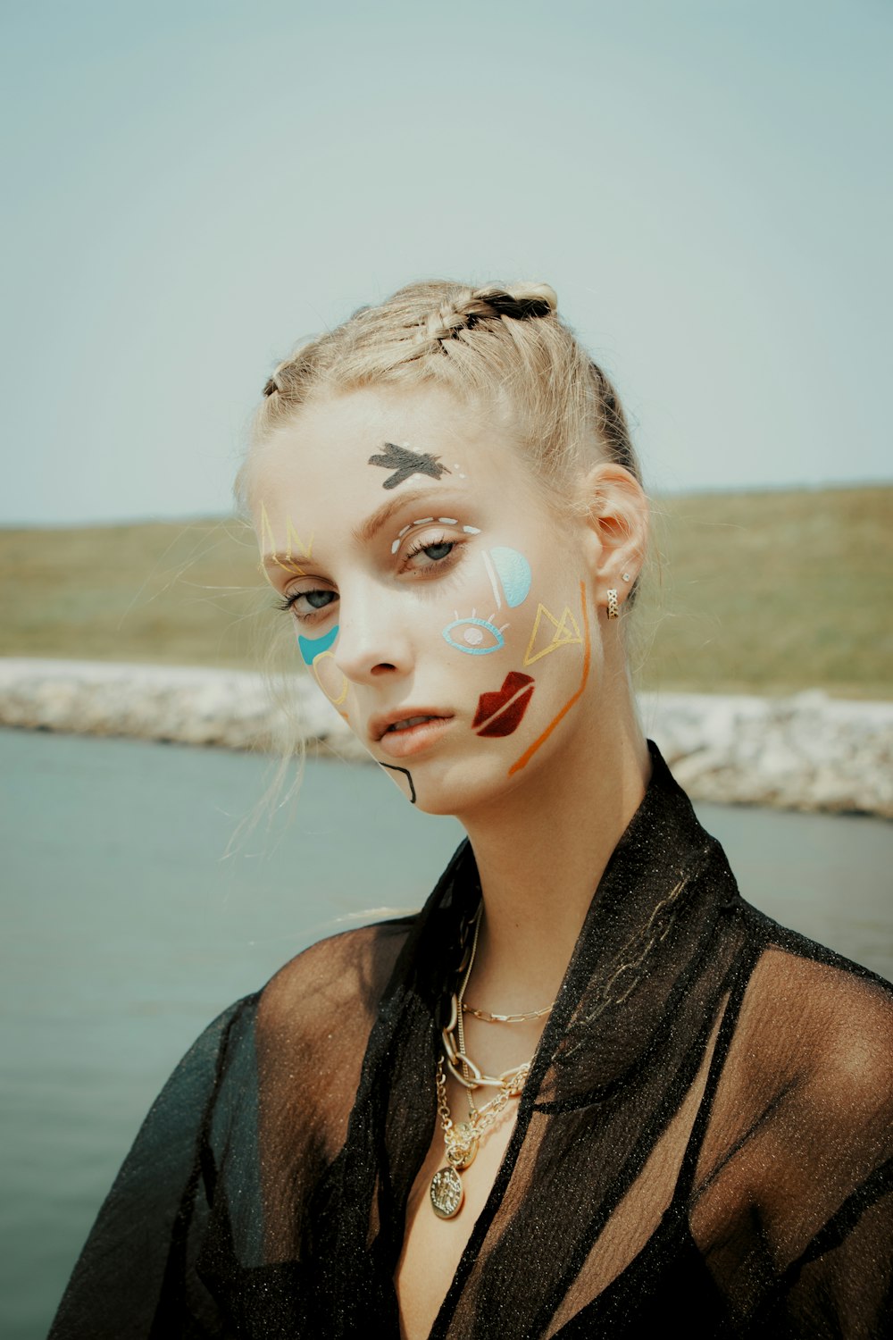 a woman with face paint on her face near a body of water