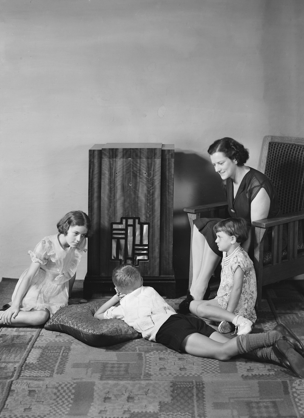 ein Schwarz-Weiß-Foto einer Frau, die mit zwei Kindern auf einem Bett sitzt