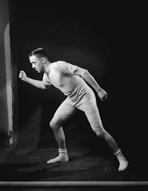 A person is wearing a vintage-style athletic outfit, composed of a form-fitting shirt and shorts, along with socks. The individual is posed in a running or athletic stance against a dark background.
