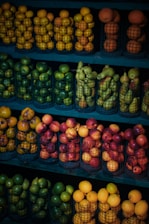 Metal baskets are filled with various types of fruit, including oranges, limes, pears, and nectarines. The baskets are arranged neatly on shelves, and the fruits are showcased in vibrant colors.