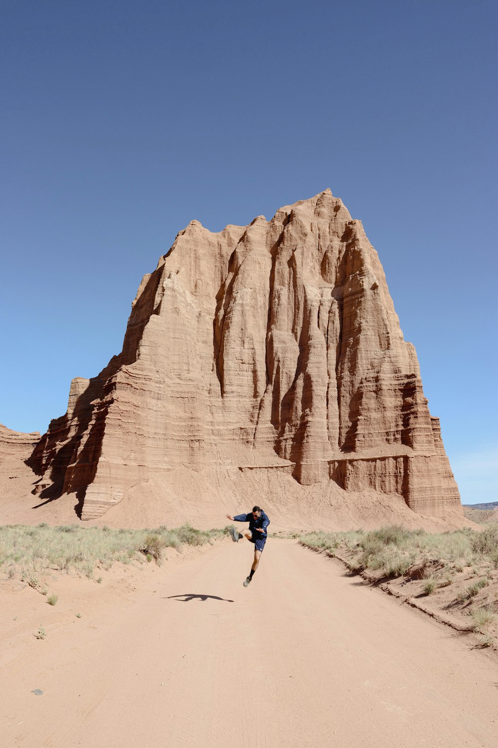 a person running across a dirt road in front of a mountain