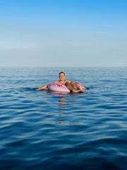 A colorful inflatable outdoor lounger floating gently on clear blue water with a bright sky above.