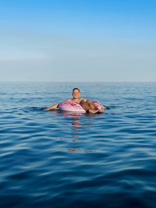 A colorful inflatable outdoor lounger floating gently on clear blue water with a bright sky above.