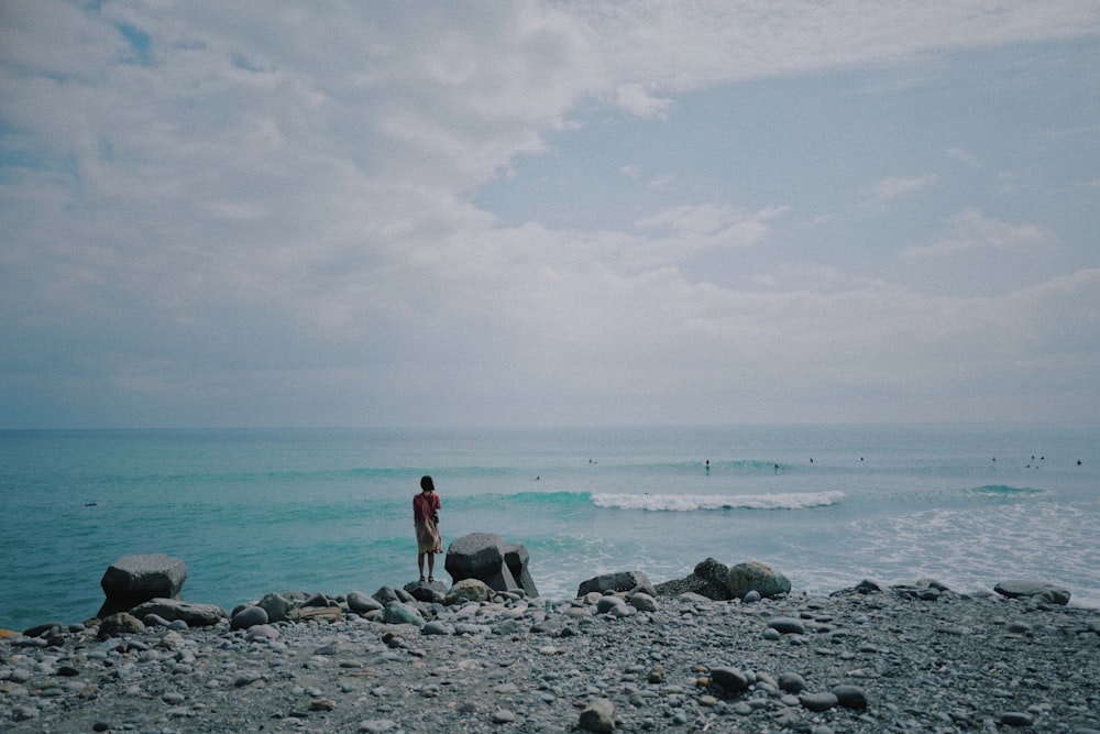 a man standing on a rocky beach next to the ocean