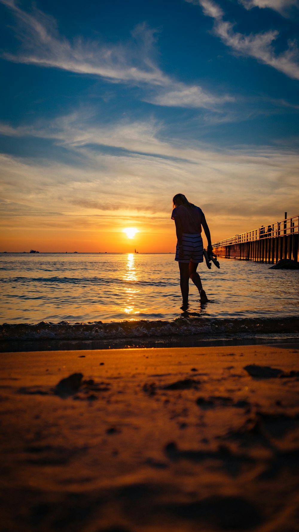 a man is walking on the beach at sunset