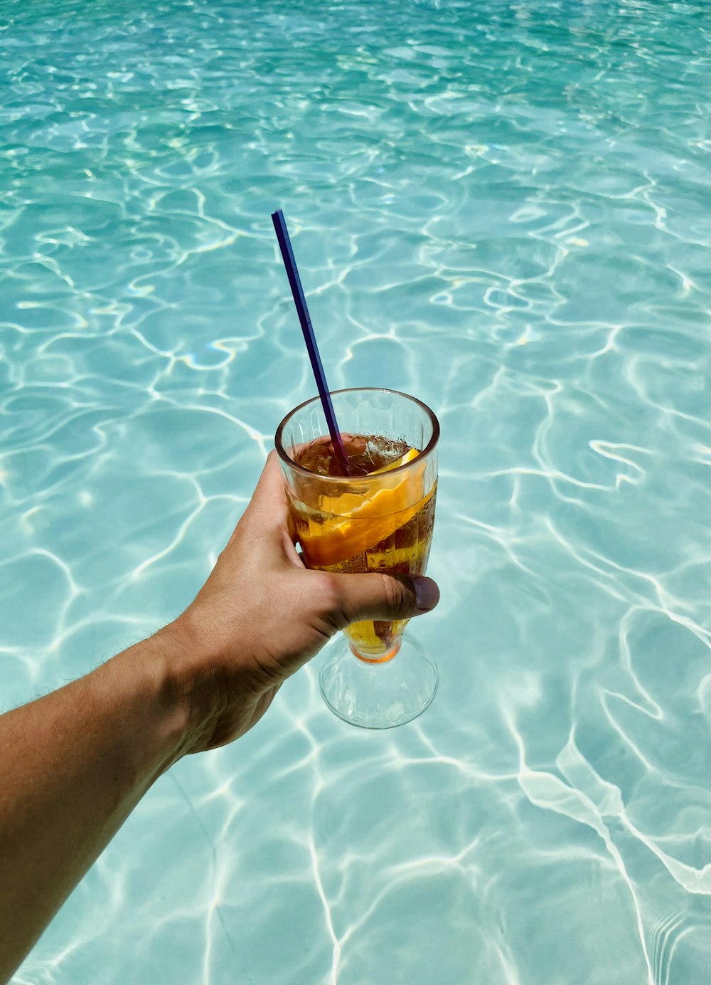 a hand holding a drink in a pool