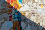 A colorful mosaic features figures engaged in various activities, including a person playing a stringed instrument and another riding a horse. The mosaic appears to tell a story with intricate details and vibrant hues, blending historical and mythical elements.