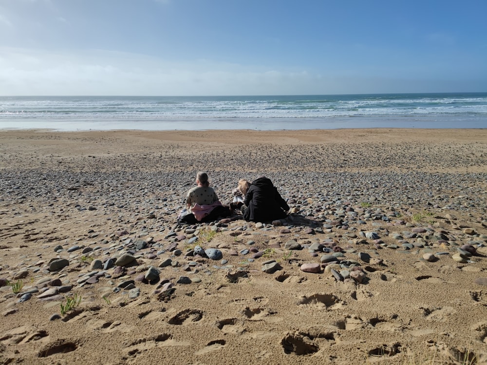 a couple of people sitting on top of a sandy beach