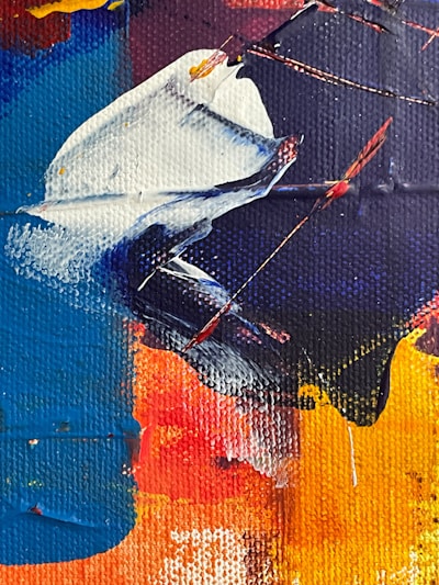 A vivid abstract painting featuring bold, sweeping strokes of color. The canvas includes rich shades of blue, red, yellow, and white, blending together to create dynamic shapes and textures. Thick, textured layers of paint are applied, with visible brushstrokes and a sense of movement and energy.