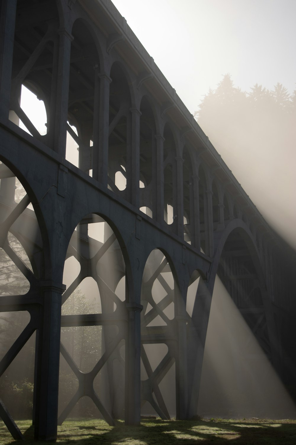 a foggy bridge with sunlight coming through the arches