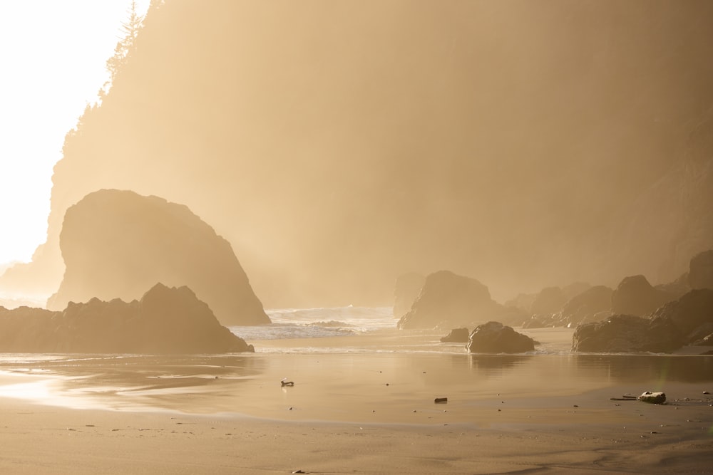 a foggy day at the beach with rocks and water