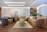 A luxurious living room features plush sofas and armchairs arranged around a central coffee table set with multiple levels. The decor includes elegant throw pillows and a soft area rug on a polished wooden floor. A wall adorned with decorative panels and a large abstract artwork serves as a backdrop. There are plants, a side table with vases, and ambient lighting that enhances the sophisticated ambiance.